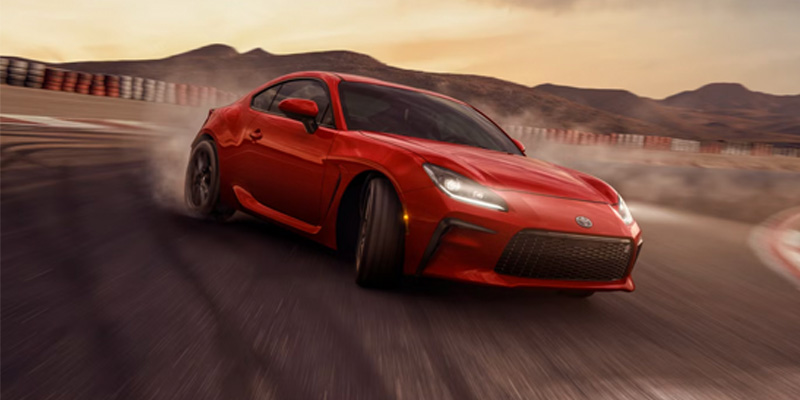 Passenger side view of a red 2025 Toyota GR86 drifting on a racetrack at dusk