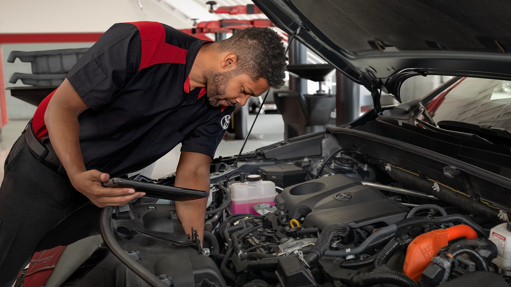 A Toyota Service Technician performing maintenance under the hood of a Toyota vehicle