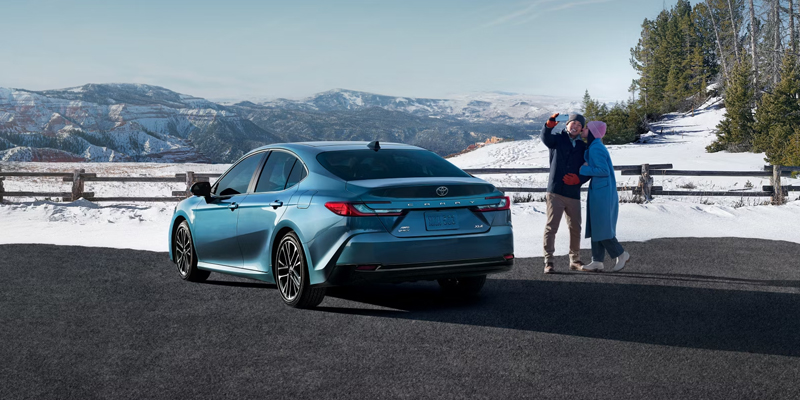 2025 Toyota Camry parked in a snowy landscape with a couple enjoying the view.