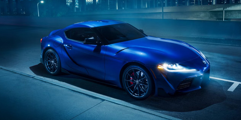 The image shows a striking 2025 Toyota GR Supra, a high-performance sports car with a sleek blue finish and dynamic design.