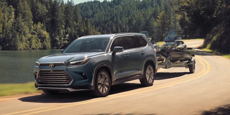 2026 Toyota Grand Highlander towing a jet ski along a scenic road.