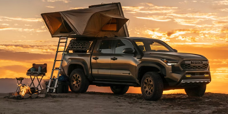 Toyota Tacoma parked at a campsite with a rooftop tent at sunset, highlighting its rugged off-road and adventure-ready design.