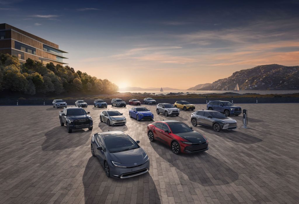 A line-up of Toyota vehicles displayed in a scenic setting, including electric models and a charging station.