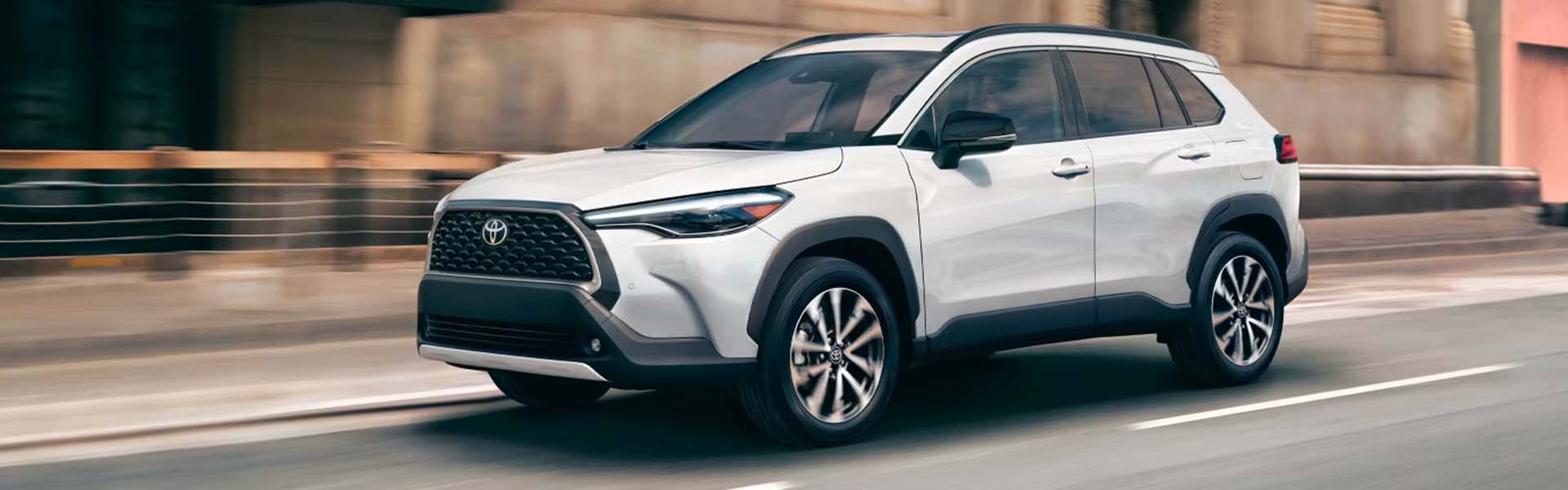 2025 Toyota Corolla Cross in white driving on a city street.