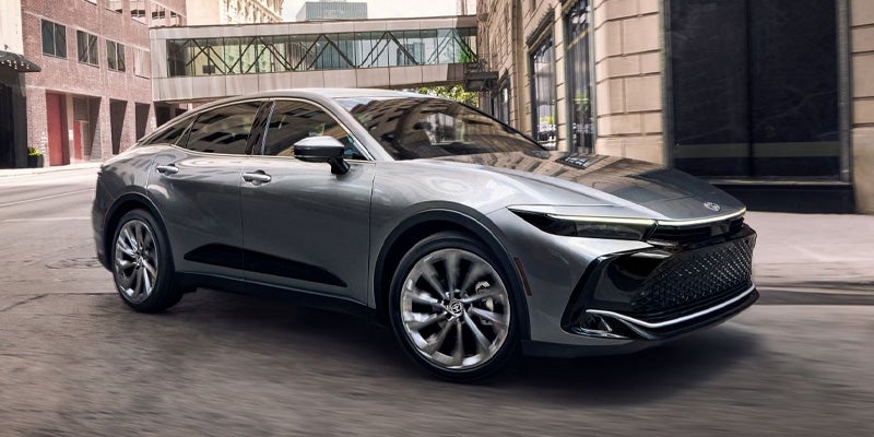 Front side view of a 2025 silver Toyota Crown driving through a modern city setting