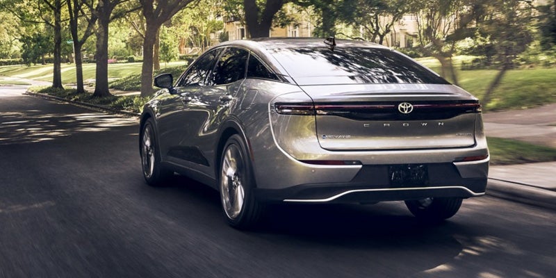 Rear view of a 2025 silver Toyota Crown driving on a tree-lined road