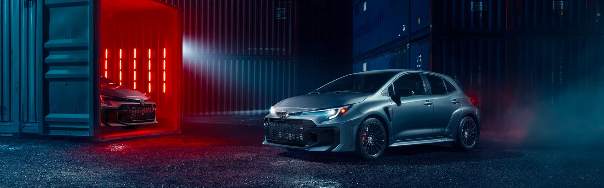 2025 Toyota GR Corolla in a dramatic lit warehouse scene with a second vehicle inside a container.