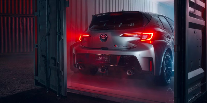 Rear view of a red 2025 Toyota GR Corolla parked inside a shipping container with dramatic lighting