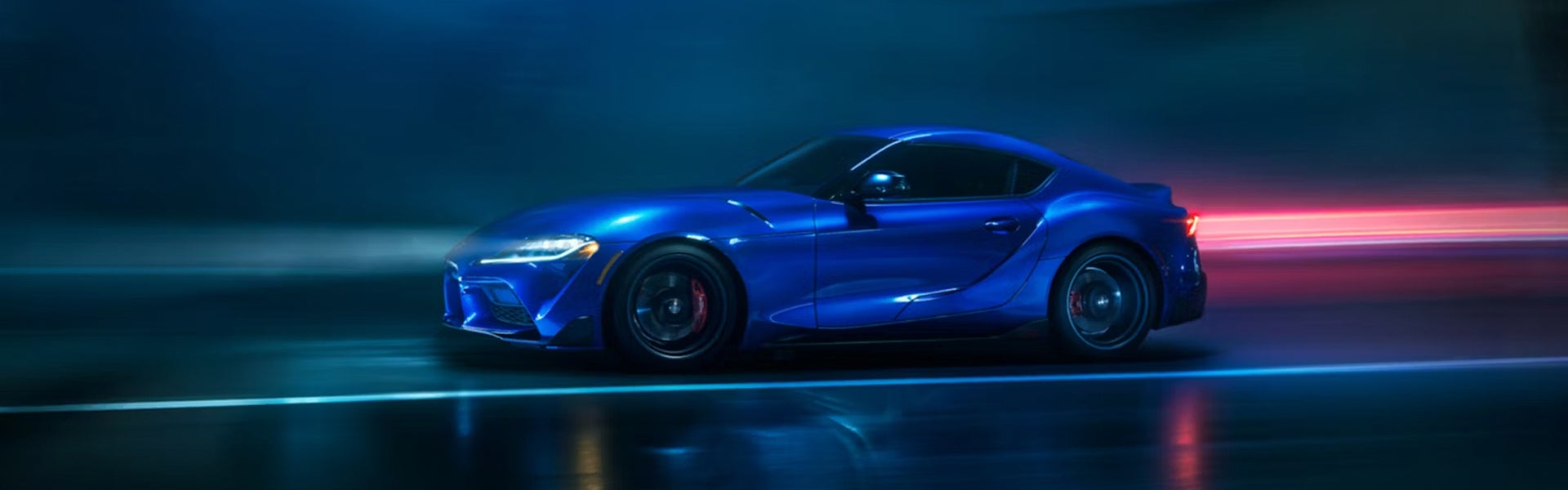 2025 Toyota GR Supra in blue racing on a night track with motion blur.