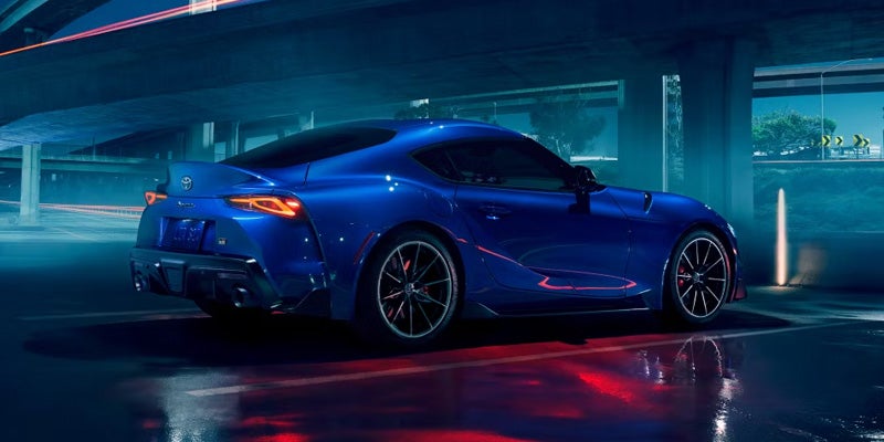 Side profile view of a 2025 blue Toyota GR Supra parked in front of a concrete wall
