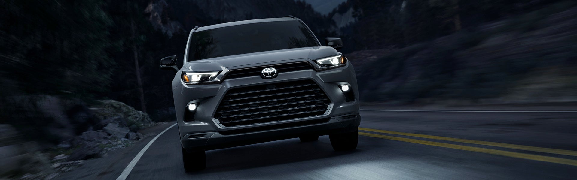 2025 Toyota Grand Highlander Hybrid driving at night on a curving road through the forest.