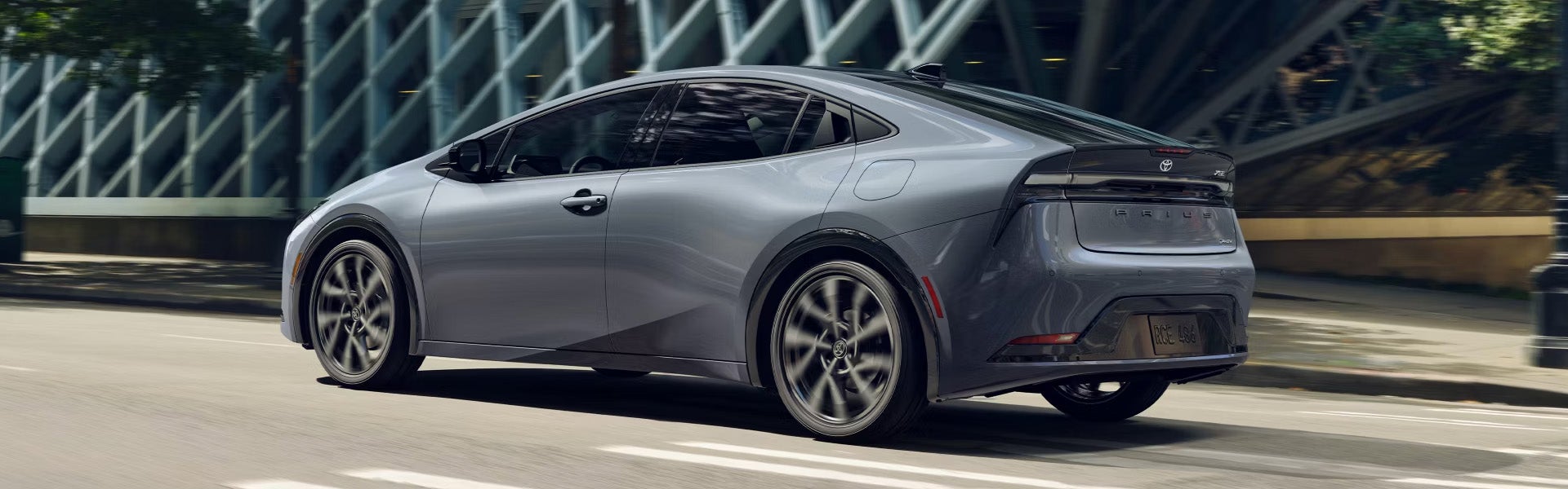 2025 Toyota Prius Plug-In Hybrid sedan driving on a city street near a modern building.