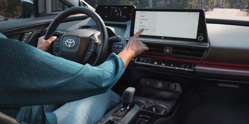 Driver using the touchscreen infotainment system inside the 2025 Toyota Prius Plug-In Hybrid