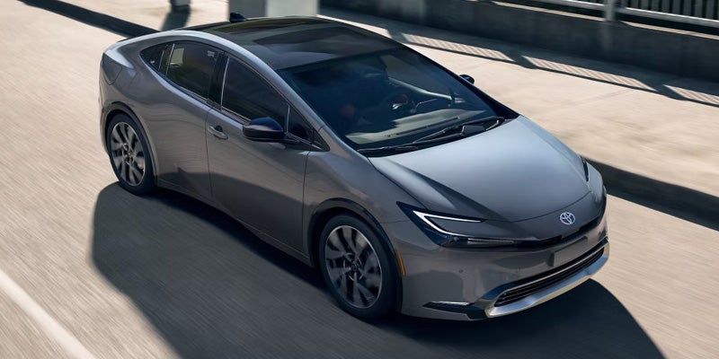 Front three-quarter view of a silver 2025 Toyota Prius Plug-In Hybrid driving on a sunny day