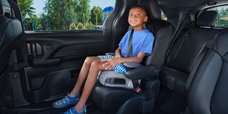 A child comfortably seated in the second-row captain’s chair of a 2025 Toyota Sienna with ample legroom and black leather upholstery.